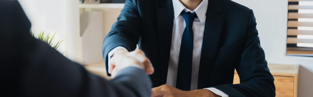 Confident businessman in suit shaking hands at office desk, symbolizing successful partnership.