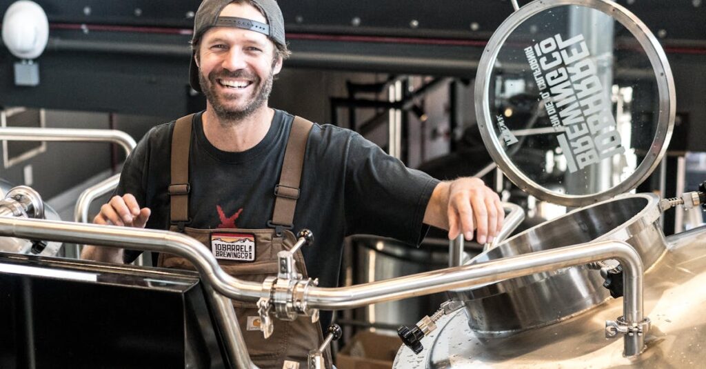 Happy brewer in a craft brewery standing near stainless steel equipment.
