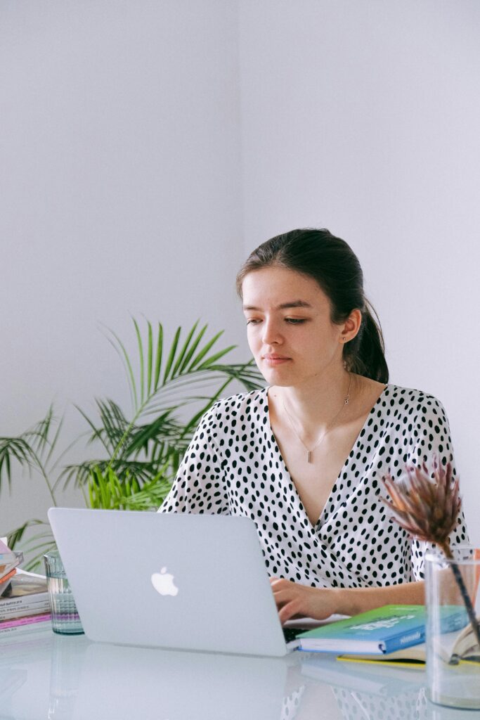 Young woman working on a laptop in a bright home office with plants and natural light.