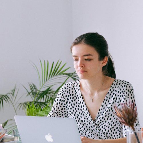 Young woman working on a laptop in a bright home office with plants and natural light.